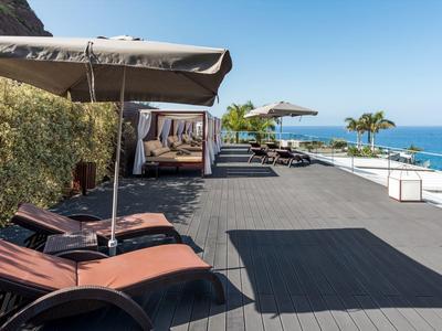 Moderne Terrasse mit Liegestühlen und Sonnenschirmen, Blick aufs blaue Meer und klaren Himmel.