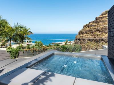 Moderner Whirlpool auf Terrasse mit Bergblick, Palmen und blauem Meer im Hintergrund.