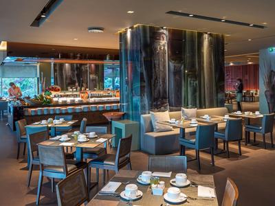 Modernes Restaurant mit blauen Stühlen, runden Tischen, großem Polstersofa und warmem Licht.