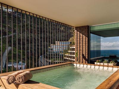 Ein Außenwhirlpool mit Holzverkleidung, zwei Handtücher liegen auf dem Rand, Berg- und Meerblick.