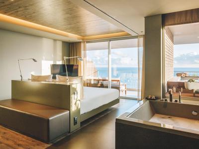 Modernes Hotelzimmer mit großem Bett, Schreibtisch, Terrasse und Blick auf das Meer.