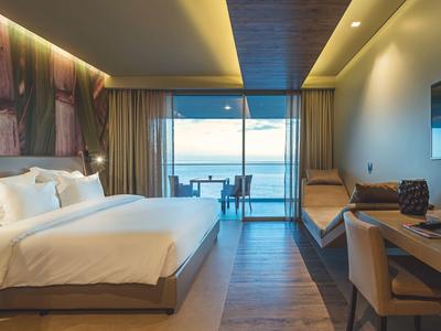 Modernes Hotelzimmer mit großem Bett, Holzfußboden, Schreibtisch und Meerblick durch große Fenster.