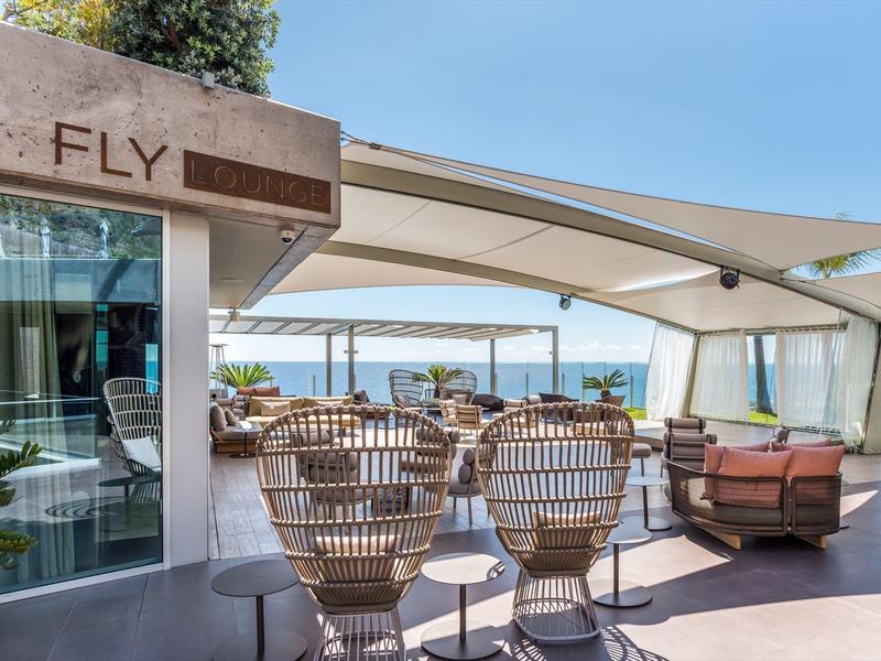 Moderner Außenbereich mit bequemen Stühlen, Tischen und Blick auf den blauen Himmel und das Meer.