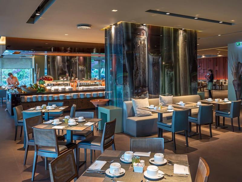 Modernes Restaurant mit blauen Stühlen, runden Tischen, großem Polstersofa und warmem Licht.