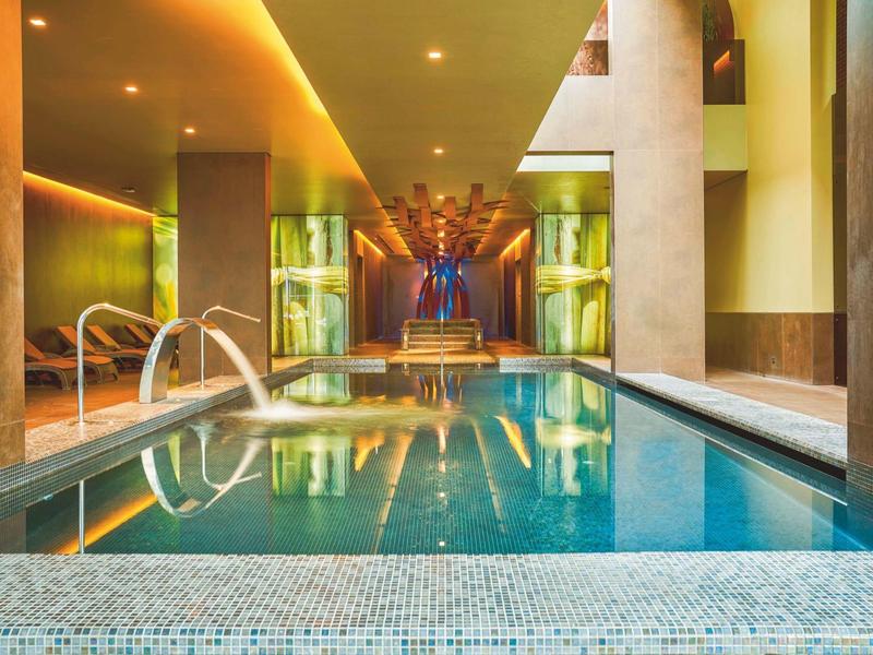 Moderner Innenpool mit warmem Licht, Glaswänden und bequemen Entspannungsbereichen neben dem Wasser.