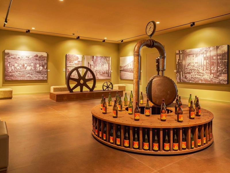 Museum mit historischen Maschinen, großen Walzen und ausgestellten kleinen Flaschen auf rundem Podest.