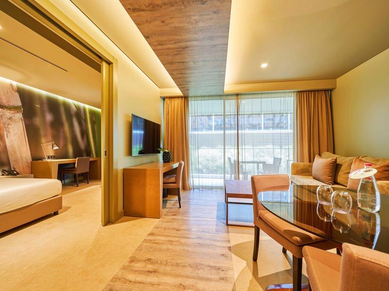 Helles Wohnzimmer mit Holzboden, Sofa, Tisch und angrenzendem Schlafzimmer mit großem Bett.