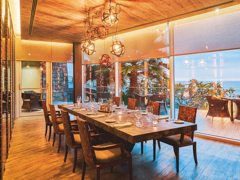 Moderner Essbereich mit großem Holztisch, sechs Stühlen und großen Glasfenstern mit Blick ins Freie.