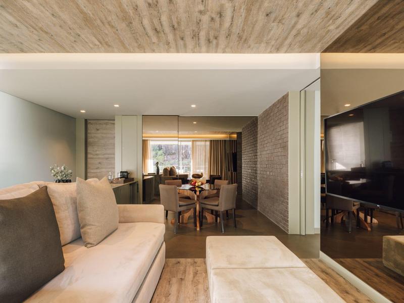 Moderner Wohnraum mit beiger Couch, großem Fernseher und offenem Essbereich in warmen Erdtönen.