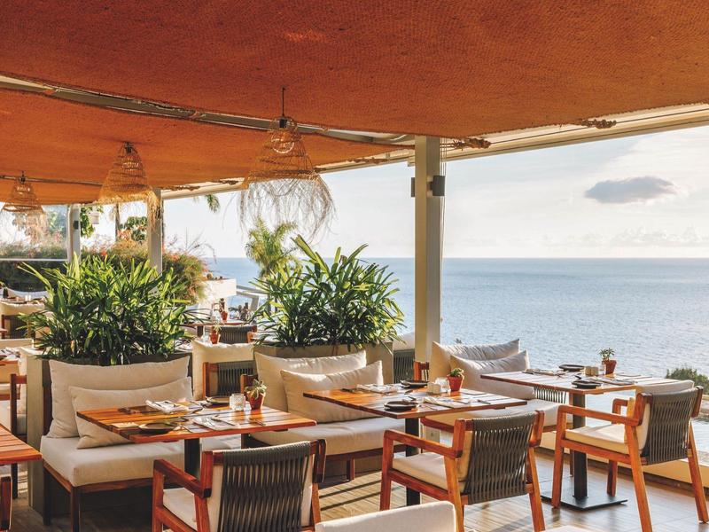 Offenes Restaurant mit Holztischen, Stühlen und Blick auf das Meer bei bewölktem Himmel.