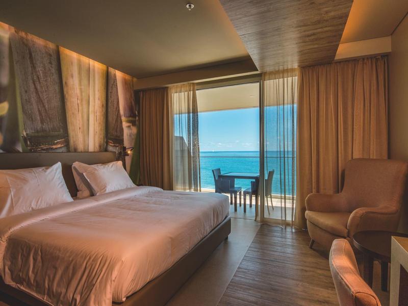 Modernes Hotelzimmer mit Doppelbett, Balkon und Meerblick, warmes Licht und gemütliche Einrichtung.