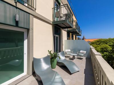 Balkon mit modernen Liegestühlen und Tisch, Teil eines Hotels bei klarem Himmel.