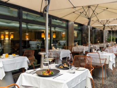 Elegant outdoor hotel restaurant with set tables and large umbrellas.