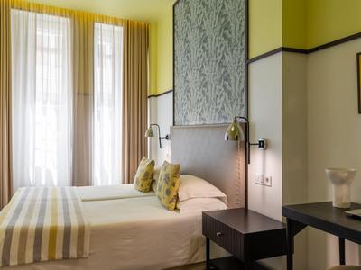 Brightly furnished hotel room with double bed, yellow curtains, and modern bedside tables.