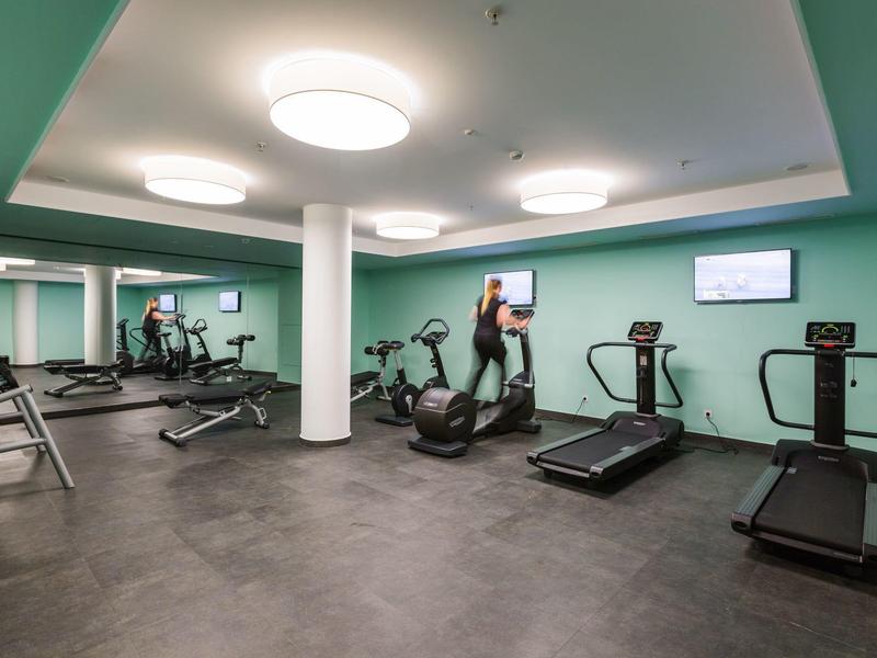 Moderner Fitnessraum mit Cardio-Geräten und grünen Wänden in einem Hotel.