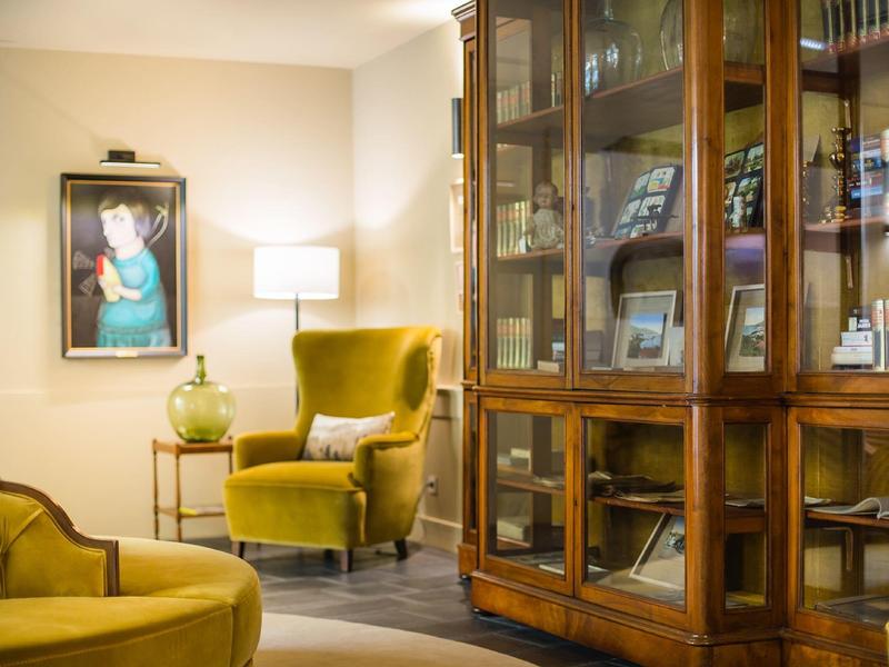 Gemütliche Ecke mit gelbem Sessel, Stehlampe und Holzvitrine voller Bücher und Gläser.