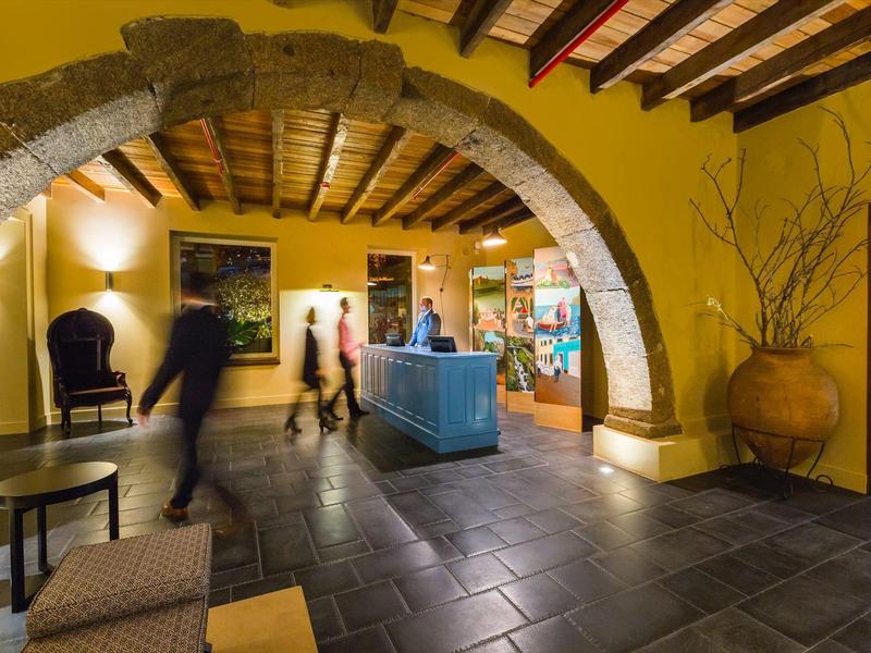 Innenraum einer warm beleuchteten Lobby mit gelben Wänden, Steinbögen und dunkelgraßen Fliesenboden.