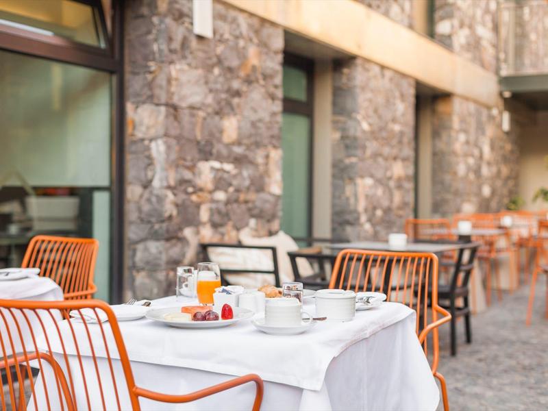 Außenterrasse mit weißen gedeckten Tischen und orangefarbenen Stühlen vor Steinmauer.