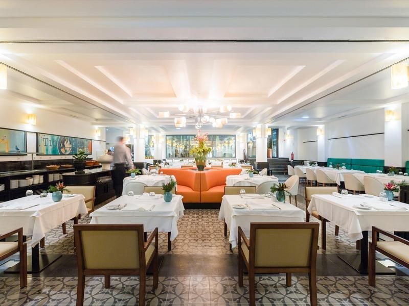 Eleganter Restaurantraum mit weißen Tischdecken, braunen Stühlen und einem orangefarbenen Sofa.