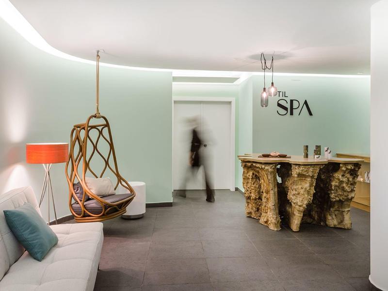 Moderner Spa-Bereich mit grünem Empfangstresen, Hängebettstuhl, Sofa und weicher Beleuchtung.