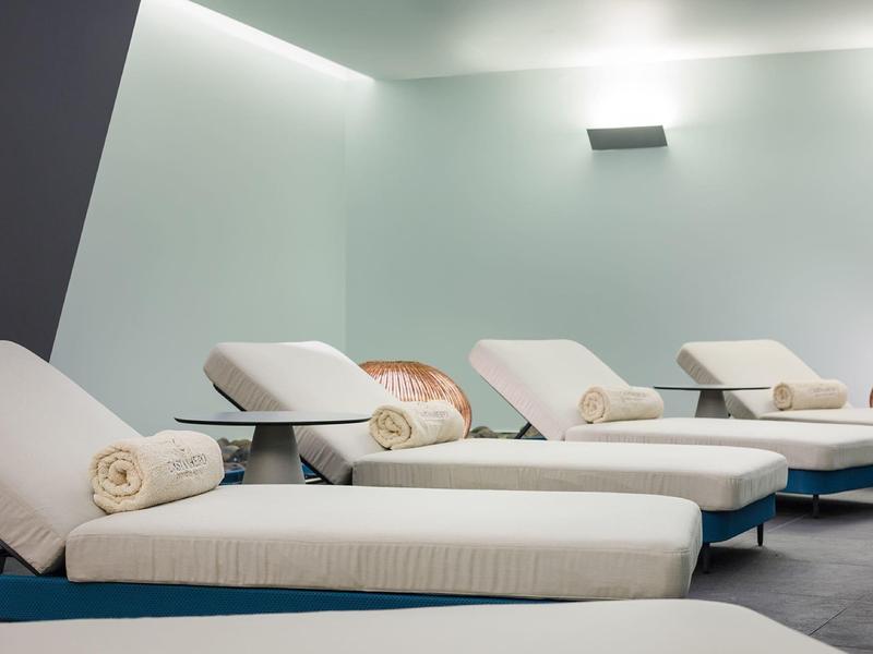 Mehrere weiße Liegen mit beige Handtüchern in einem hellen, modernen Ruheraum stehen nebeneinander.