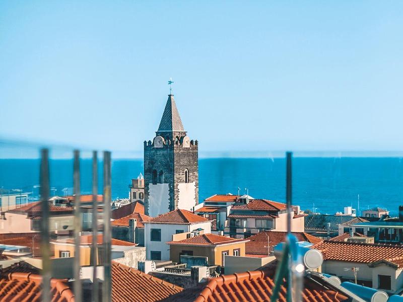 Stadt mit roten Dächern, Kirchturm und blauem Meer im Hintergrund bei klarem Himmel.