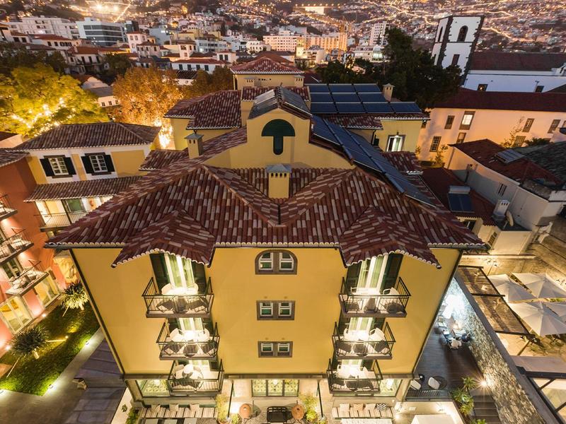 Blick auf ein gelbes Wohnhaus mit Ziegeldach und Balkonen in einer dicht bebauten Stadt bei Nacht.