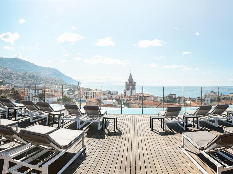 Große Terrasse mit Liegestühlen und Meerblick, bewölkter Himmel, Berge im Hintergrund.