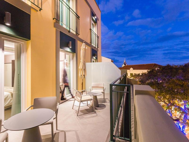 Moderner Balkon mit Stühlen und Tisch, gelbe Hauswand, blaue Abendhimmel mit Wolken.