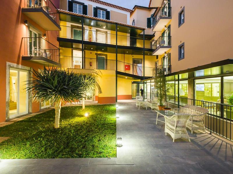 Moderne Innenhofterrasse mit Sitzmöbeln, Beleuchtung, Glasfassade und grasbewachsenem Bereich.