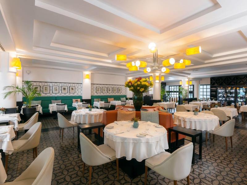 Großes, elegantes Restaurant mit runden Tischen, weißen Tischdecken und bequemen Stühlen.