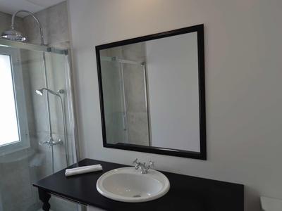 Nowoczesna łazienka z umywalką, dużym lustrem i prysznicem oświetlonym światłem dziennym.