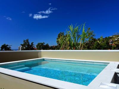 Przejrzysty basen na zewnątrz z białą krawędzią pod niebieskim niebem i zielonymi roślinami.