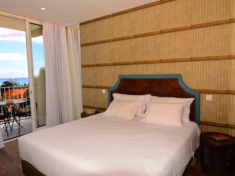 Pokój hotelowy z dużym łóżkiem i balkonem z widokiem na morze w świetle dziennym.