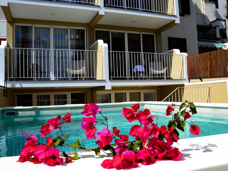 Różowe kwiaty na brzegu czystego basenu przed wielopiętrowym hotelem.