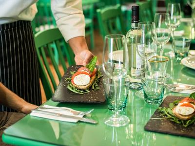 Un camarero sirve un plato cuidadosamente presentado sobre una mesa verde en un restaurante.