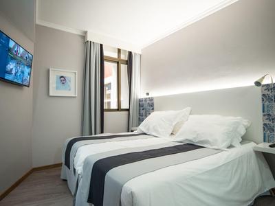 Habitación de hotel moderna con cama doble, televisor en la pared y luz natural desde la ventana.