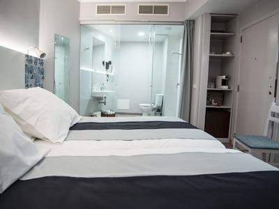 Dormitorio con cama doble junto a un baño con pared de cristal en habitación de hotel moderna.