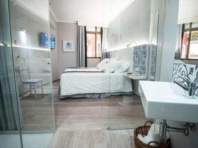 Habitación de hotel moderna con cama doble, ducha de vidrio y lavabo grande en diseño claro.