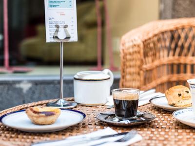 Taza de café y pastel en una mesa tejida al aire libre con un menú al fondo.