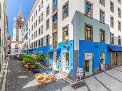 Pouliční kavárna vedle bílého domu s modrými akcenty a kostelní věží v pozadí.