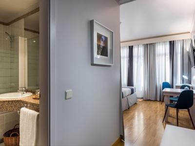 Pasillo de habitación de hotel moderna con vista al baño y área de estar con piso de madera y grandes ventanas.
