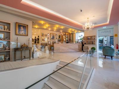 Lobby de hotel luminosa con mármol blanco, escaleras, recepción y iluminación elegante.
