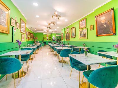 Restaurante luminoso con paredes verdes, sillas de terciopelo azul y mesas con jarrones de flores.