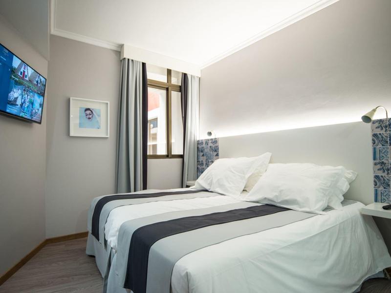 Habitación de hotel moderna con cama doble, televisor en la pared y luz natural desde la ventana.