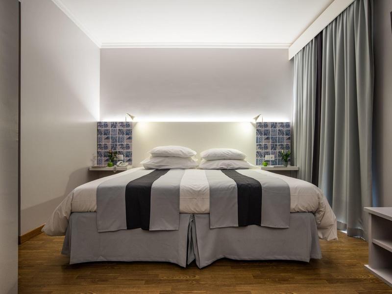 Habitación de hotel moderna con dos camas individuales, cortinas grises y piso de madera.