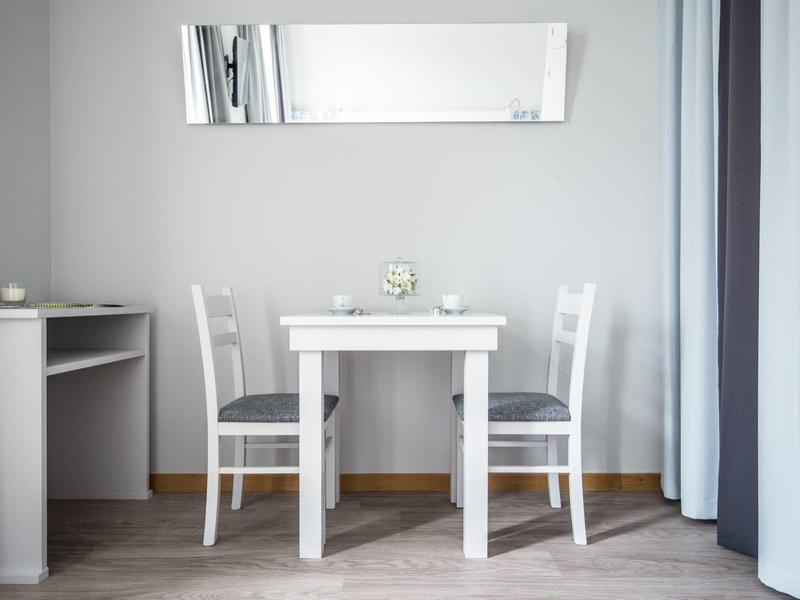 Mesa blanca pequeña con dos sillas en una habitación clara y minimalista.
