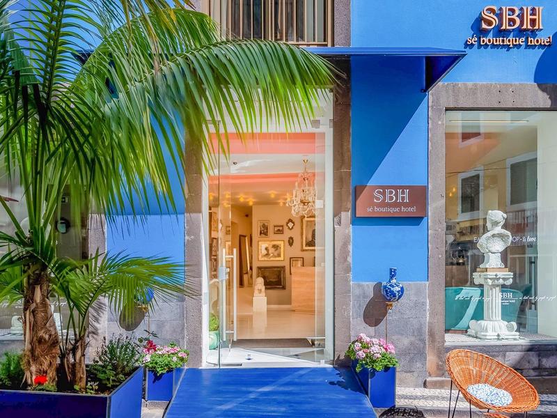 Entrada de hotel con paredes azules, plantas y una acogedora zona de asientos al aire libre.