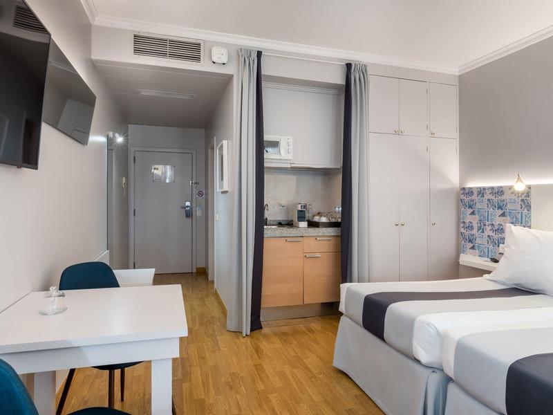 Habitación de hotel moderna con cama doble, escritorio, televisión y zona de cocina pequeña.