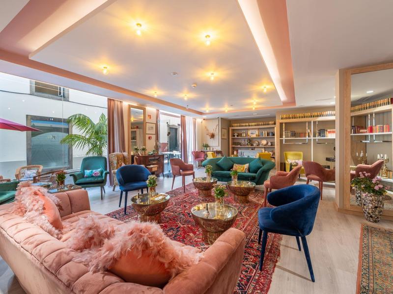 Habitación de hotel elegante con sofás cómodos, sillas coloridas y luz cálida.